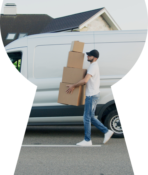 A man carrying a stack of boxes in front of a white van.