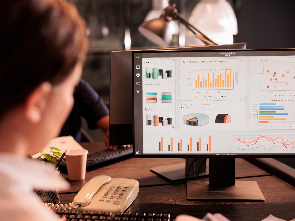 A woman sitting in front of a computer screen with graphs and charts on it.