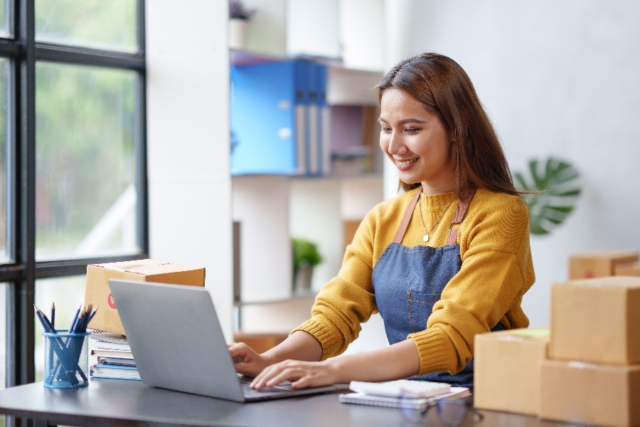 A woman in a yellow shirt is typing on a laptop.