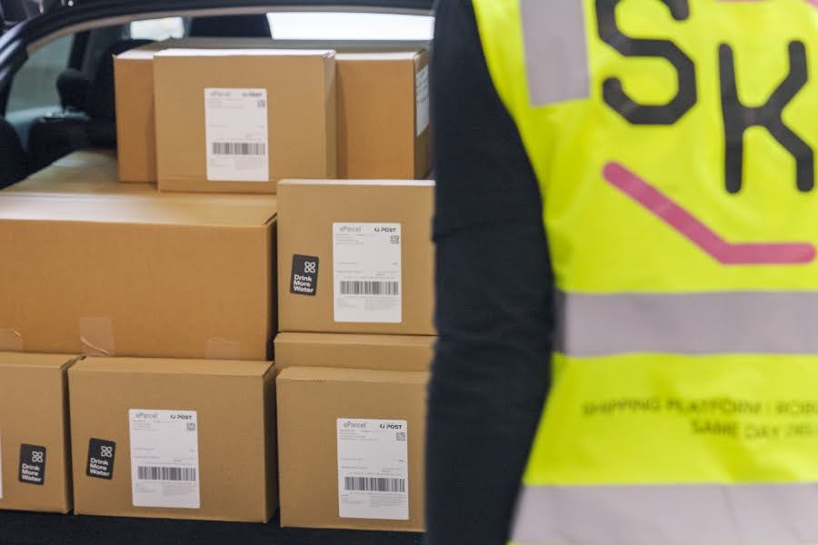 A person wearing a yellow vest is standing next to a pile of boxes.