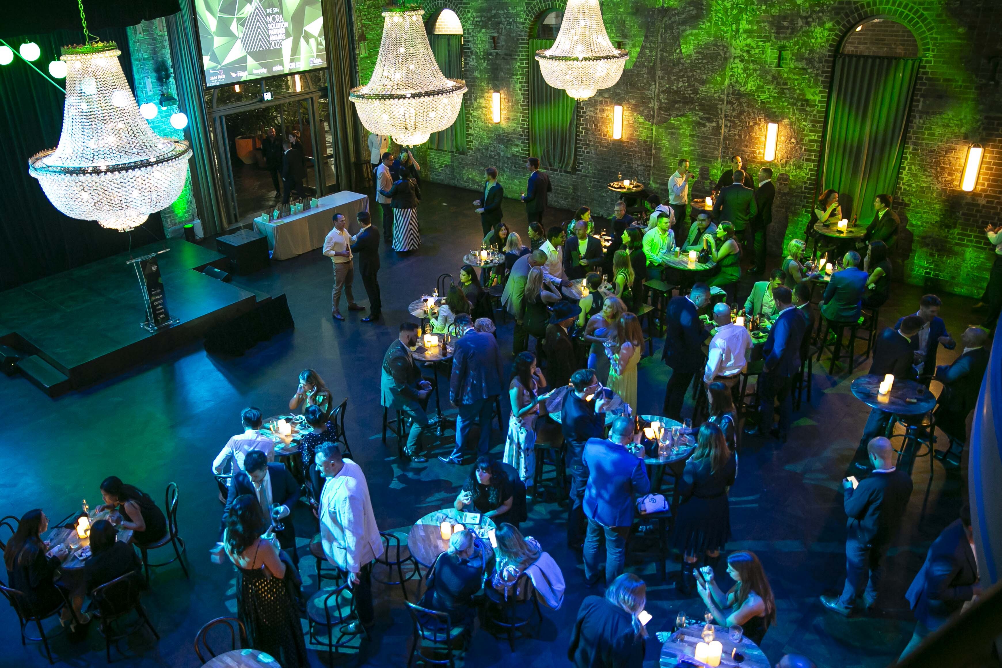 A large group of people are gathered in a room with chandeliers and tables.