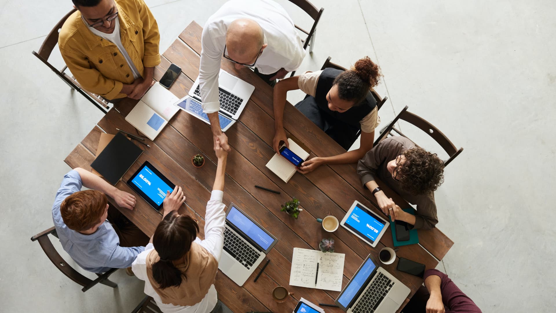 A group of people sitting around a table with laptops and cell phones.