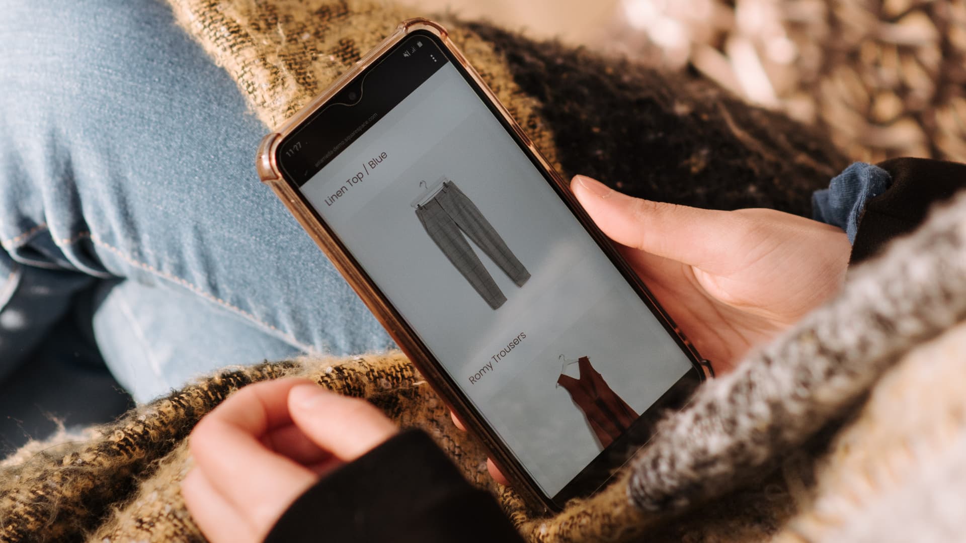 A person holding a cell phone with a screen displaying a clothing store.