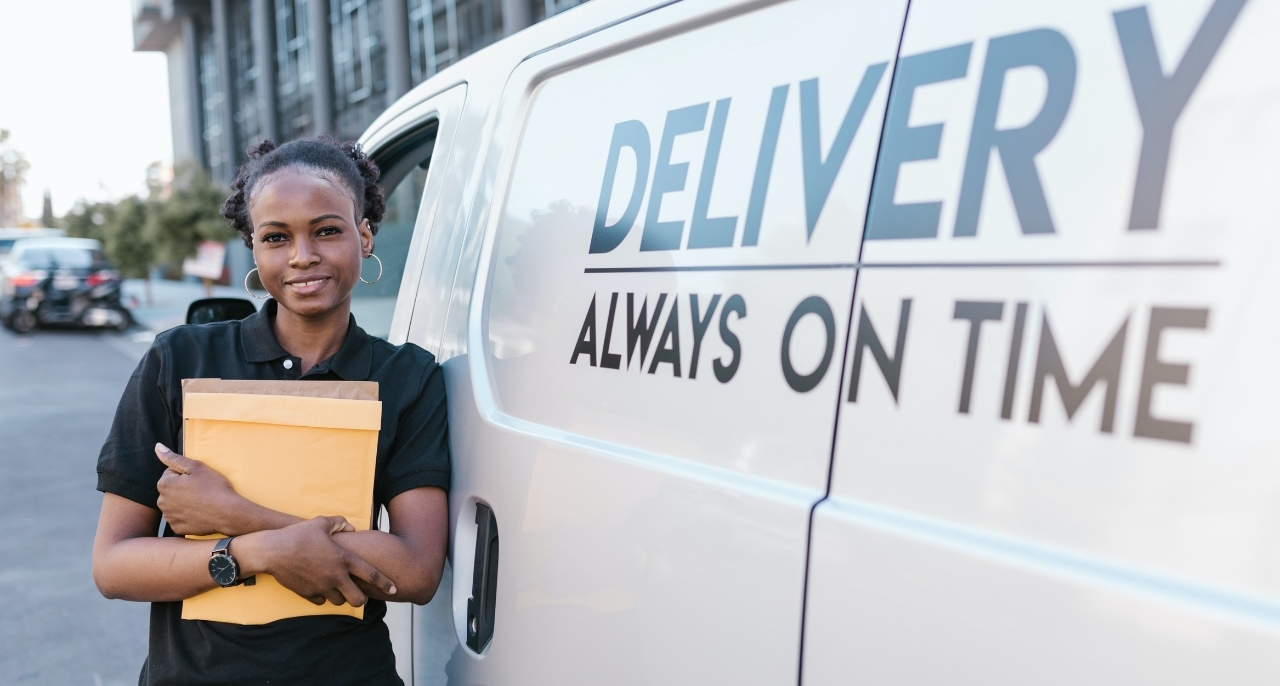 A woman standing in front of a white van with a box in her hand.