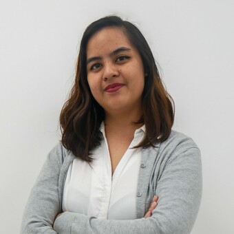 Woman in a white shirt and grey cardigan with arms crossed, standing confidently.