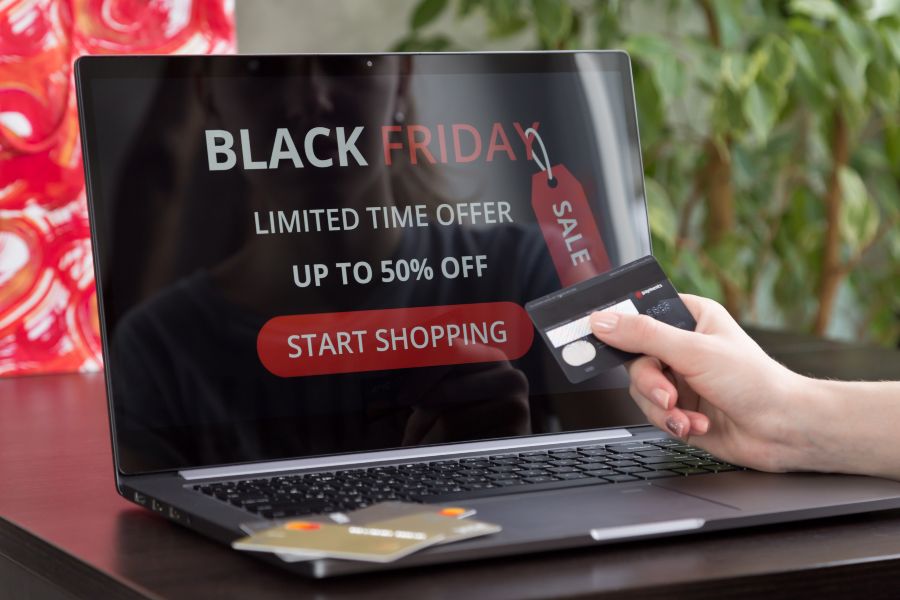Online shopper holding credit card at laptop showing Black Friday sale ad with discounts.
