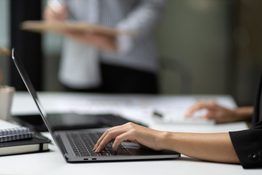 Business professional typing on laptop during meeting, planning BFCM sales strategy.