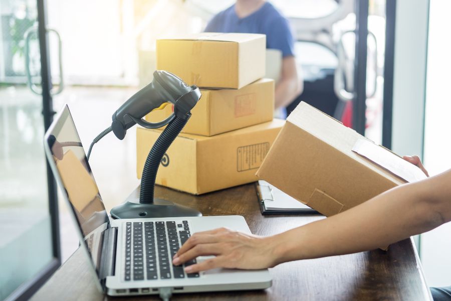 Business owner scanning and entering parcel details into order fulfilment software on laptop.