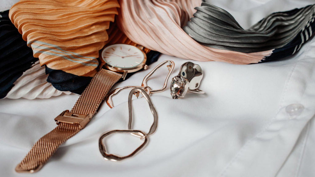A watch and a pair of earrings are on a white cloth.