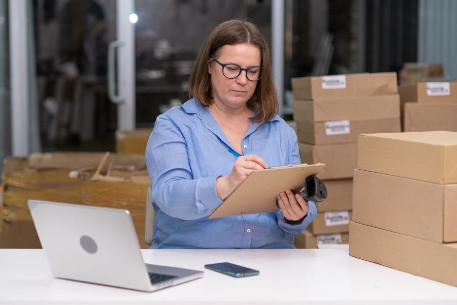 Woman reviewing packages and documents, highlighting RMA’s role in business and tech.