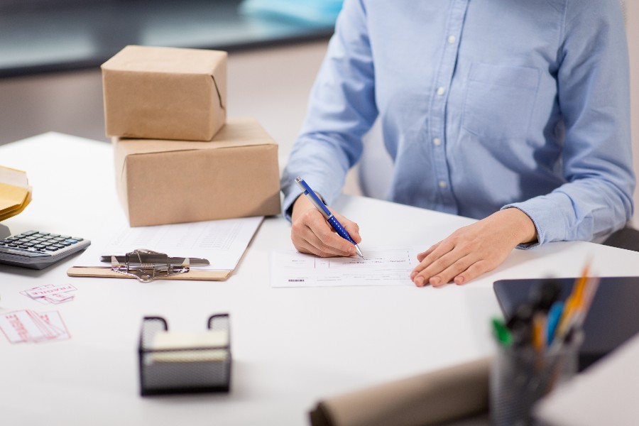 Worker filling out order documents beside cardboard packages in an office setting.