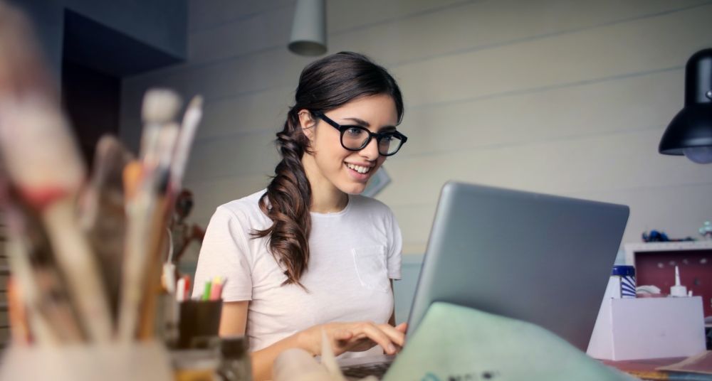 A woman with glasses is typing on a laptop.