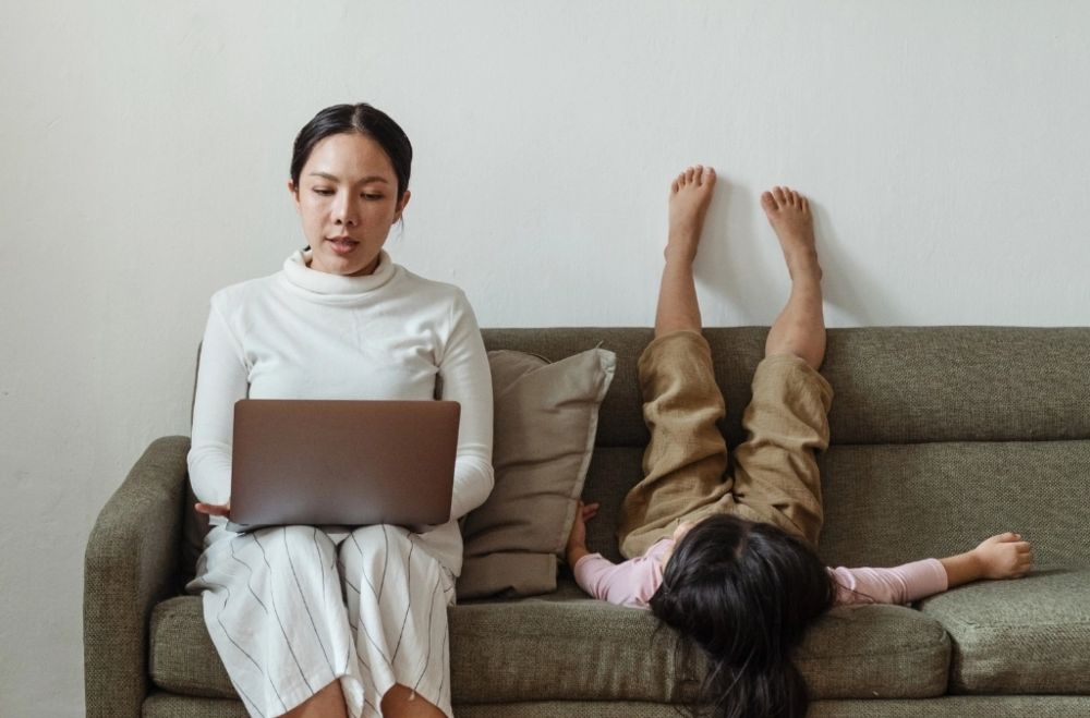A woman sitting on a couch with a laptop and a child sitting on her lap.