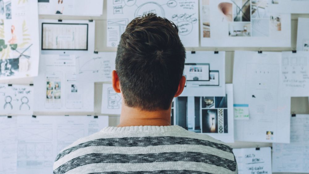 A man with a striped sweater looking at a bulletin board.