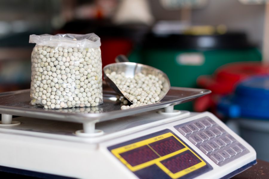 Bag of peas and metal scoop being weighed on a digital scale for net and gross weight comparison