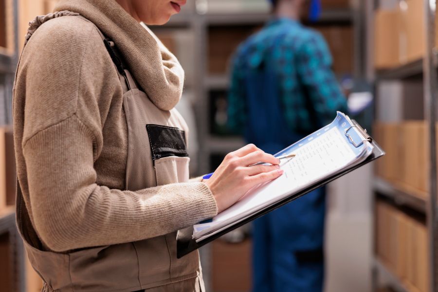 A woman in a white shirt is writing in a clipboard.