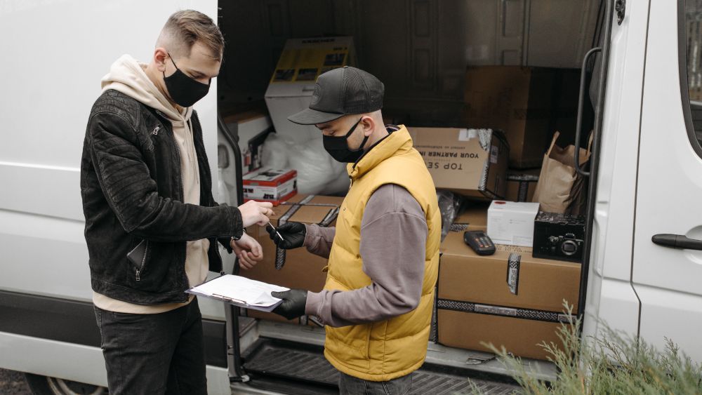 Two men in a truck with boxes and one of them wearing a yellow vest.