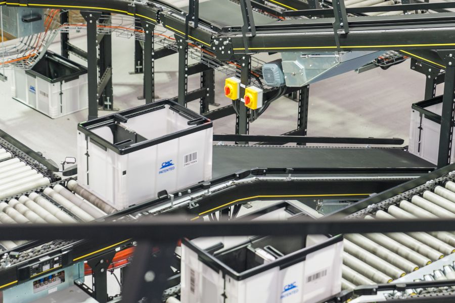 Automated conveyor system moving plastic totes through a modern warehouse sorting facility.