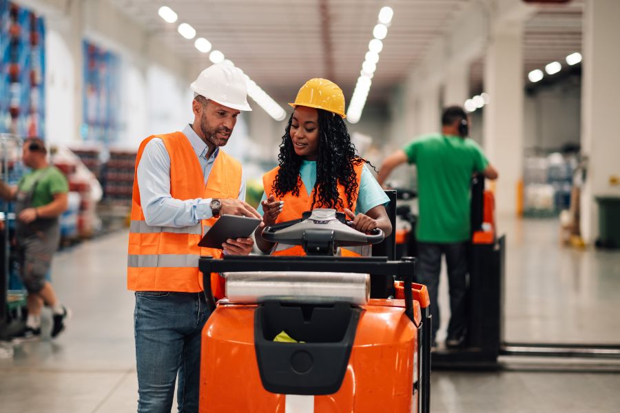 Two workers in orange vests are using a tablet computer.