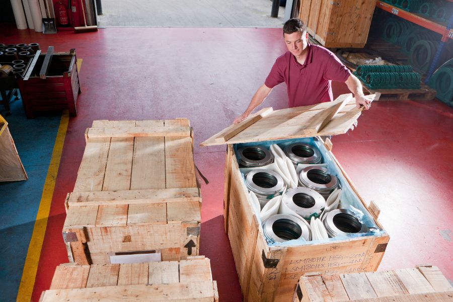 Warehouse worker closing a wooden crate filled with protected metal parts ready for shipping.