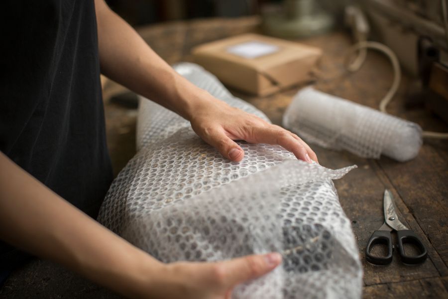 Hands wrapping a product in bubble wrap on a workbench, preparing protective shipping dunnage.