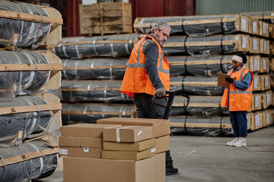 Warehouse workers in safety vests moving stacked boxes and checking shipments for dunnage mistakes.
