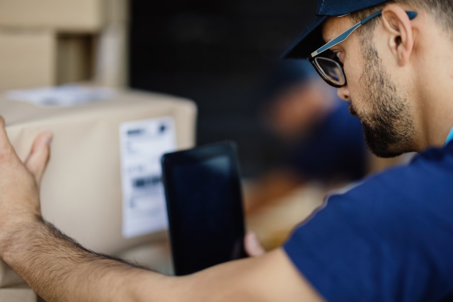 Delivery courier scanning barcode on cardboard box label with handheld device.