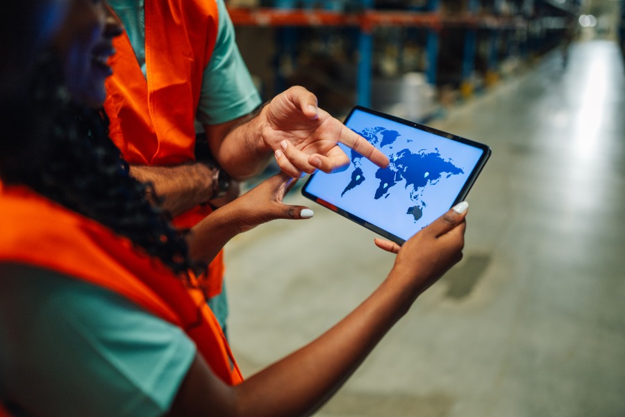 Warehouse workers reviewing world map on digital tablet for global supply chain planning.
