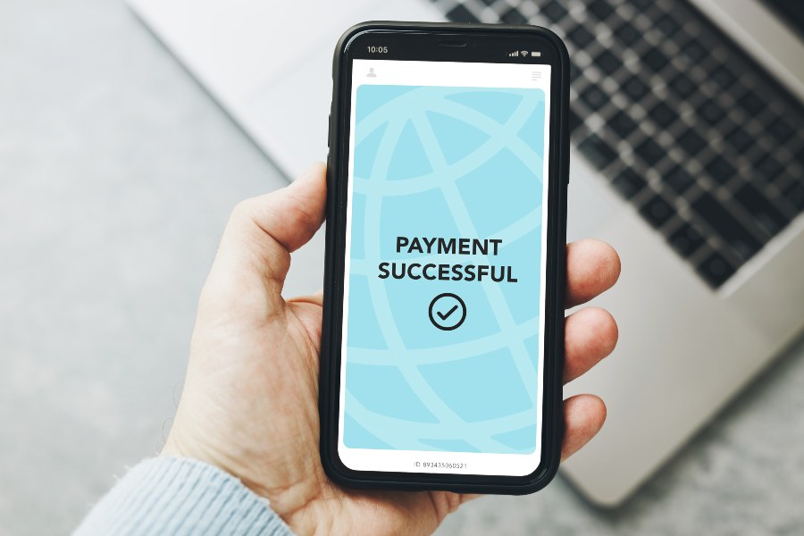 Hand holding smartphone with “Payment successful” screen, illustrating pay-as-you-go fulfilment costs.
