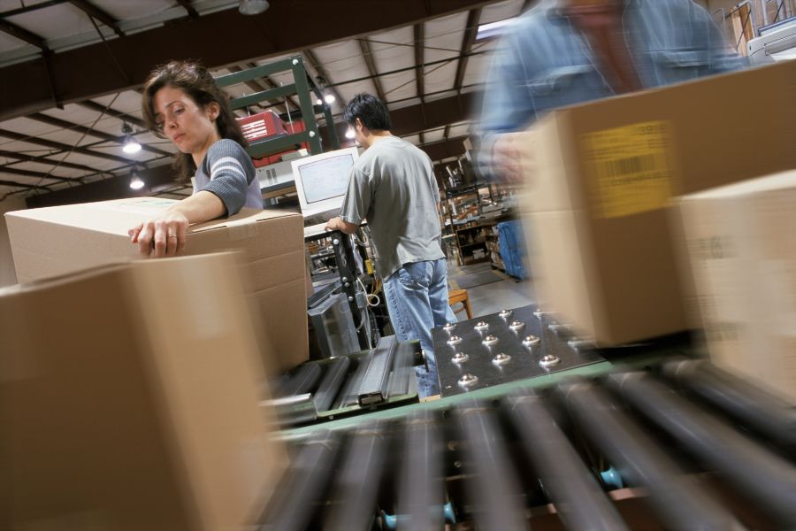 Motion-blurred warehouse workers lift boxes onto conveyor belts for efficient 3PL operations.
