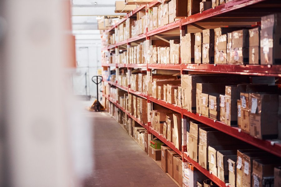 Warehouse storage room filled with boxes on red racks and pallet truck.
