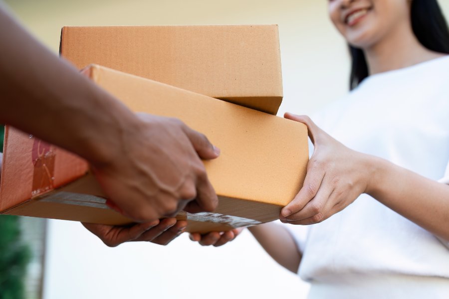 Delivery person hands package to smiling woman outside home entrance.