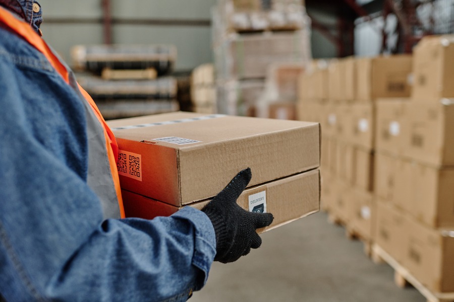 Warehouse worker carries boxes in a busy distribution aisle.