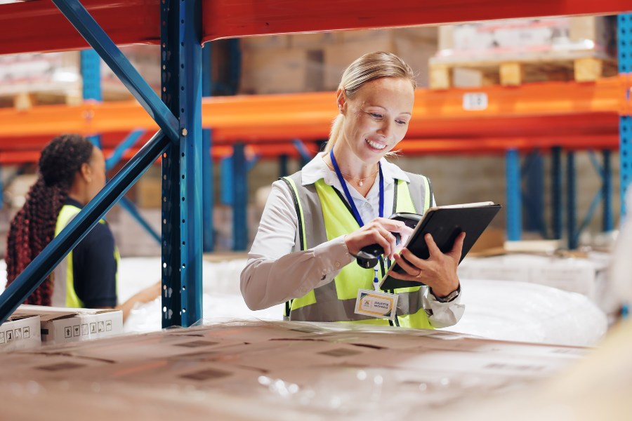 A warehouse worker using a tablet and scanner beside stacked boxes in a warehouse.