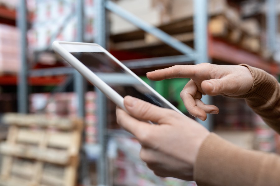 A hand using a tablet in a warehouse setting.