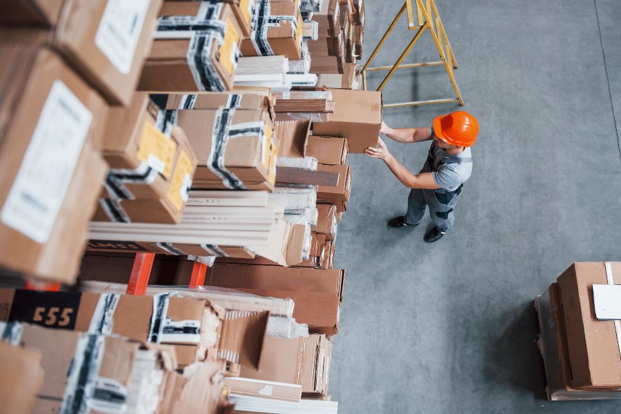 A warehouse worker handling a box in a large storage aisle, seen from above.