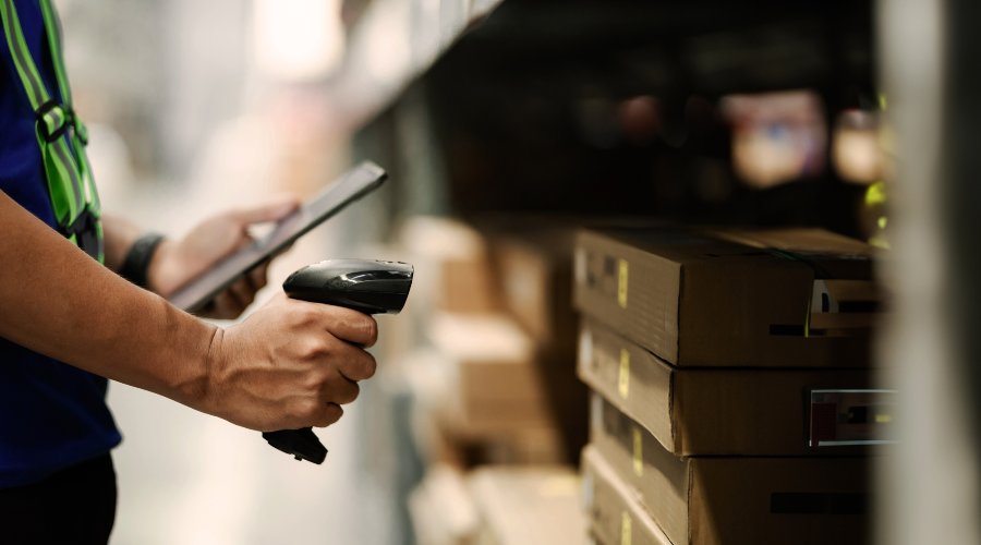 A person scanning a barcode with a tablet beside stacked boxes in a warehouse.