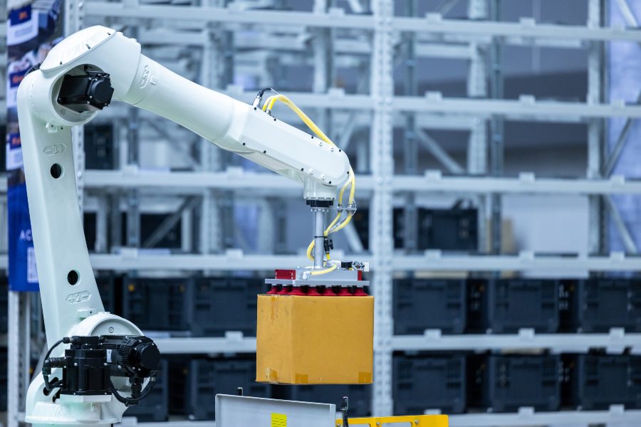 White robotic arm using vacuum gripper to lift box in warehouse automation setup