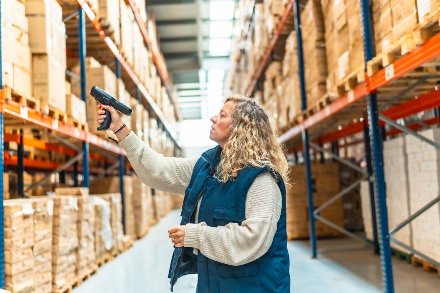 Warehouse worker using RF scan reader to track high-volume stock on shelving aisles
