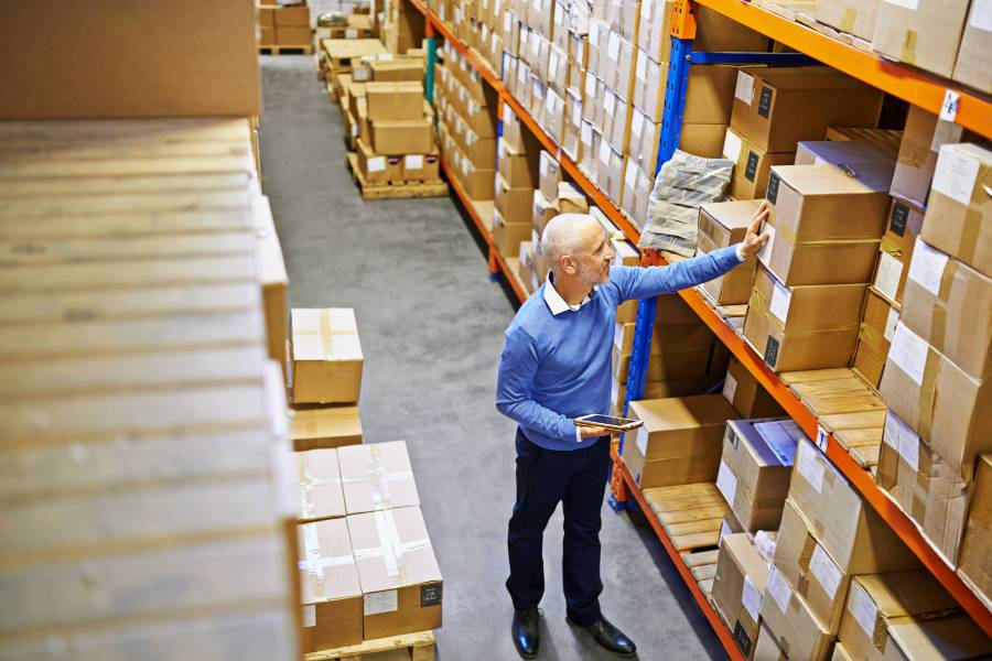 Warehouse manager with tablet checking boxed stock on shelving racks, intro to preventing stockouts and calculating safety stock