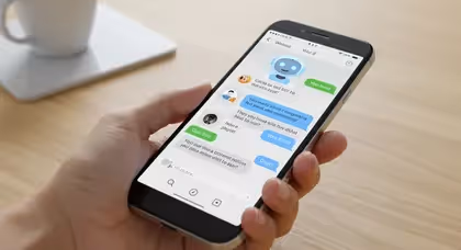 Mão segurando smartphone com conversa de chatbot em aplicativo de mensagens