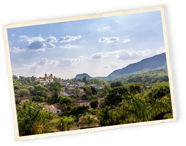Scenic view of a small town with white houses and a church surrounded by lush greenery and hills under a partly cloudy blue sky.