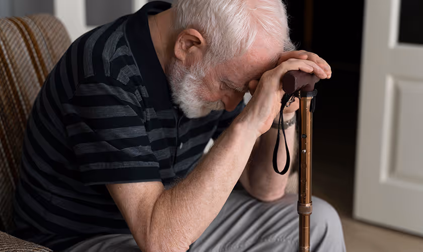 Homme senior assis, tête baissée sur sa canne, exprimant fatigue et détresse après un AVC. Illustration du besoin d’accompagnement au quotidien.