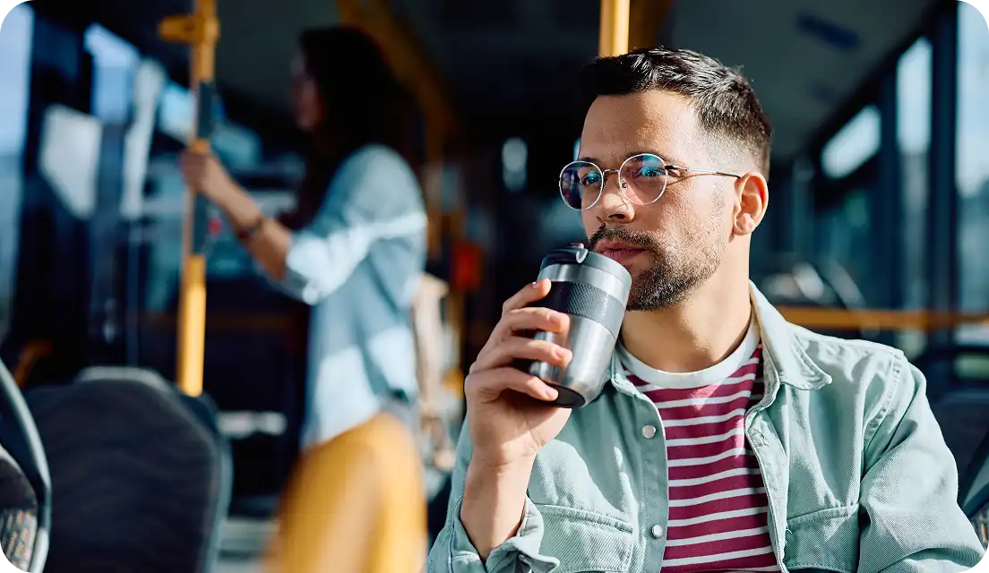 Young woman wearing wireless earbuds and a black blazer, looking at her smartphone indoors with yellow lighting in the background.