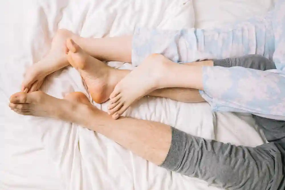 Couple lying under the sheets in bed with only their intertwined legs exposed.