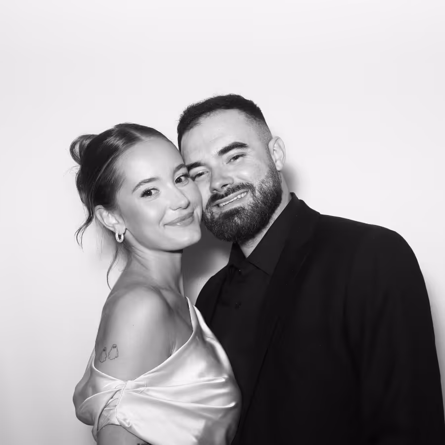 Smiling couple close together, woman in satin off-shoulder dress and man in dark jacket with beard.