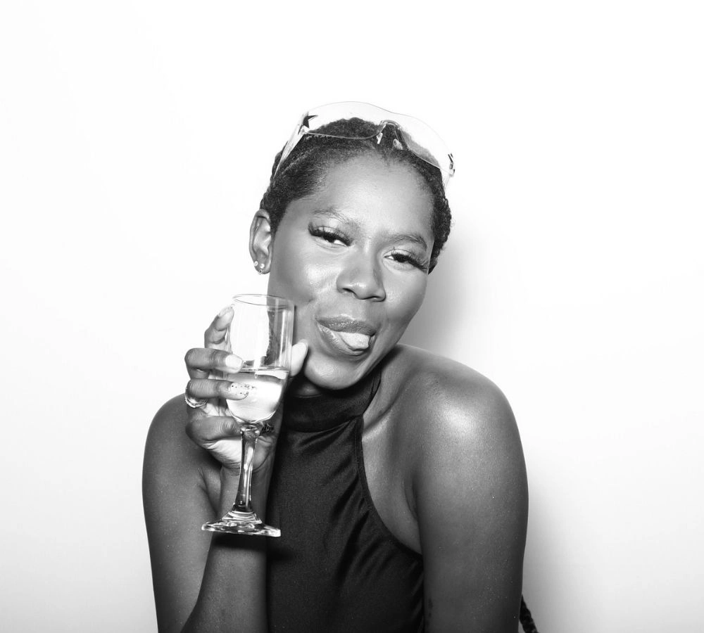 Four women dressed in glam outfits posing in black and white with oversized sunglasses and fun photo booth accessories