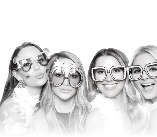 Four women posing in a photo booth with glitter backdrop, wearing Happy New Year headbands and festive outfits