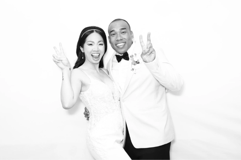 Bride and groom smiling and making peace signs against a white background.