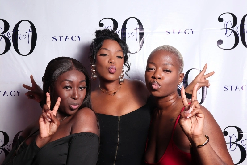 Three women posing in front of a white backdrop with '30 Strict Stacy' text, all making peace signs and puckering their lips.